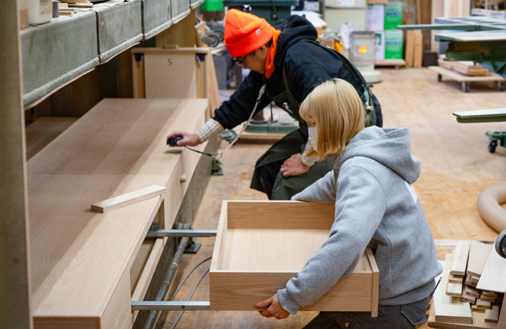 Two craftspeople at YATSUKI WOODWORKS assembling a wooden fixture in the workshop.
